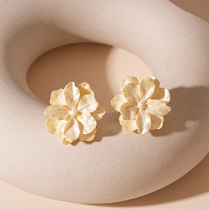 Vue détaillée des boucles d'oreilles fleurs en acrylique beige sur un support mat texturé