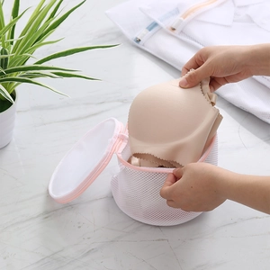 Cylindrical mesh laundry bag for bras, hands placing lingerie in a pink trim washing net