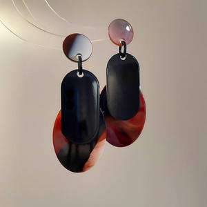 Détail de boucles d'oreilles géométriques en acrylique aux motifs ambre et rouge