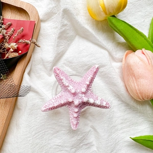 Close-up of pink starfish phone grip with realistic 3D texture on a white fabric base