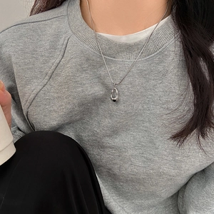 Close-up of a silver minimalist irregular teardrop pendant necklace on a grey sweater