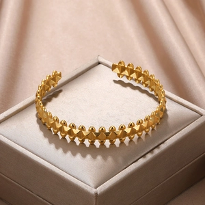 Detail of gold open cuff bracelet with geometric pyramid studs on silk background
