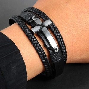 Close-up of multi-layer black braided leather bracelet with a metal cross charm on wrist