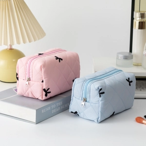 Quilted cotton cosmetic bags with black bow patterns in pink and light blue on a desk