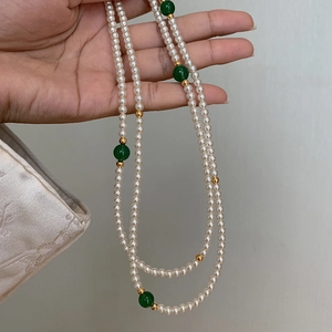 Elegant pearl necklace with green beads and gold accents held in hand on gray background