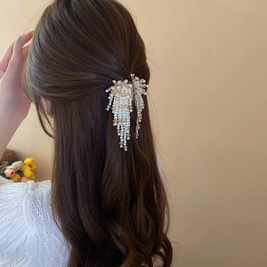 Elegant side view of a faux pearl tassel hair claw clip worn on long wavy brown hair