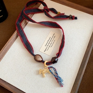 Detail of vintage necklace with gold pendant and red blue tassel on a wooden tray