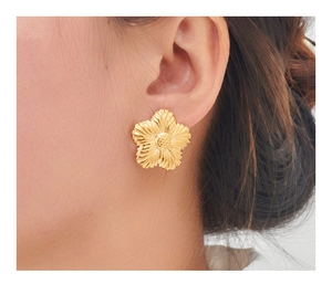 Détail macro d'une boucle d'oreille fleur dorée avec pétales texturés sur un mannequin