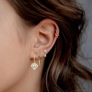 Close-up of a model wearing a set of gold earrings with green zircon and flower studs