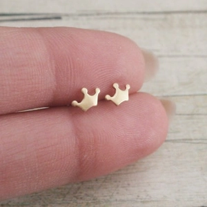 Minimalist golden crown stud earrings with a matte satin finish held in hand