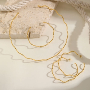 Macro detail of golden wave-shaped hoop earrings on natural stone textures with soft shadows