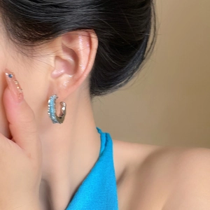 Gros plan sur la boucle d'oreille C en cristal bleu portée avec aiguilles en argent