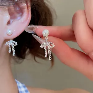 Elegant pearl stud earrings with delicate silver lace bow pendants worn on a female ear