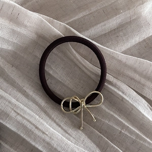 Detail of dark brown elastic hair tie with a vintage golden metal bow on fabric background