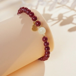 Detailed view of red beads bracelet with white bead and golden gourd-shaped lucky charm