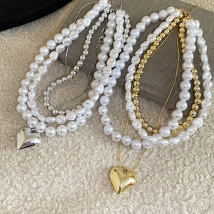 Détail de colliers de perles multicouches avec pendentifs en forme de cœur dorés et argentés
