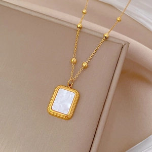 Detail of 18k gold plated chain with square white shell pendant on silk background