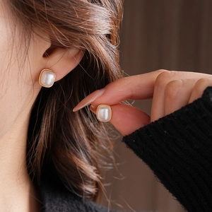 Close-up of elegant square pearl earrings with gold metallic edge on woman's ear