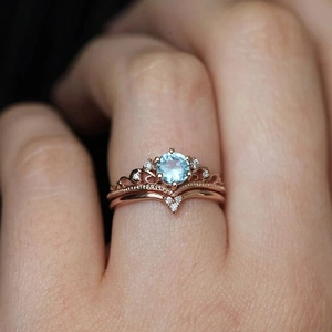 Macro detail of stacking rose gold rings featuring a crown design and blue round zircon