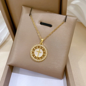 Detailed close-up of golden cross necklace with white shell inlay and sparkling crystals