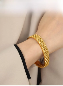 Detailed view of a gold-plated link bracelet with a textured watch strap design on wrist