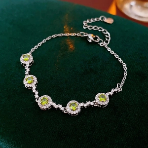 Detailed view of silver link bracelet with five green zircons on dark green velvet
