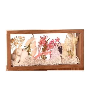 Handmade wooden frame with dried flowers and wedding figurines on white background