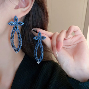 Detail of a model wearing a geometric bow earring with blue zircon and long drop pendant