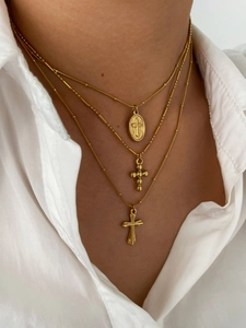 Close-up of a triple-layered gold cross necklace with religious charms on a white shirt