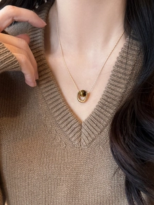 Macro shot of U-shaped gold necklace with brown tiger eye stone on brown sweater