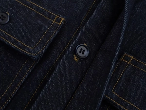 Détails du tissu denim indigo brut avec coutures contrastées et boutons noirs