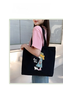 Outdoor shot of a black canvas tote bag with cartoon girl and cat illustration