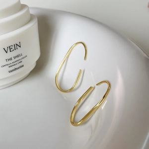 Minimalist gold U-shaped oval hoop earrings displayed on white ceramic plate with soft light