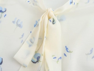 Dettaglio camicetta in chiffon giallo chiaro con stampa floreale e fiocco al collo