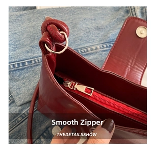Detail view of smooth zipper and magnetic buckle on burgundy PU leather shoulder bag