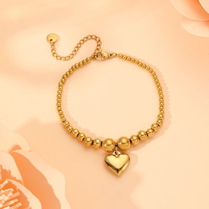 Close-up of golden heart pendant bead bracelet on a soft pink background with paper flowers