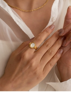 Close-up of elegant gold ring with oval white mother of pearl on a model's finger