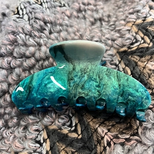 Detail of large marble teal hair claw clip with golden flecks on knit fabric