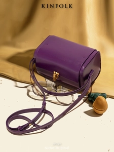 Détail du fermoir rectangulaire doré sur un sac bandoulière cylindrique en cuir violet