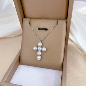 Detail of a pearl cross pendant on a silver chain displayed in a luxury gift box