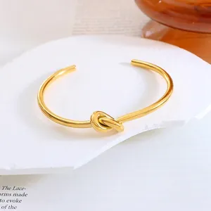 Polished gold knot open cuff bracelet in titanium steel displayed on a stone plate