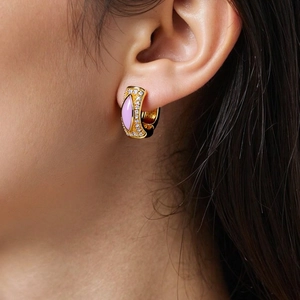 Detailaufnahme eines Goldohrrings mit rosa Emaille und Zirkonia am Ohr des Models