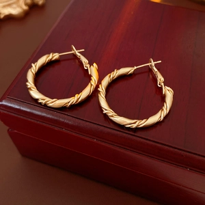 Close-up of golden twisted hoop earrings with a matte finish on a vintage wooden box