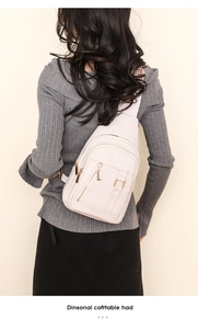 Detail of light beige PU leather chest bag with gold zippers worn over a grey sweater