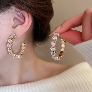 Detail view of gold C-shaped hoop earrings with sparkling rhinestones on the ear