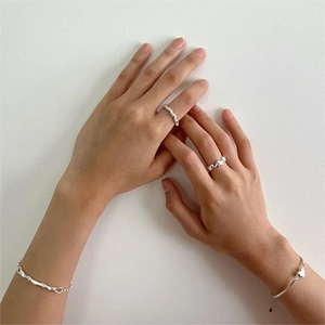 Detail of silver knot ring and heart bracelet on model hand with minimalist background