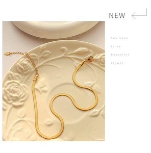 Detail of a gold flat snake chain with lobster clasp and engraved oval logo tag on a ceramic plate