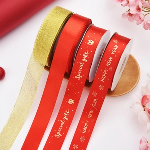 Detail of red and gold Christmas ribbons with Happy New Year foil print on a wooden tray