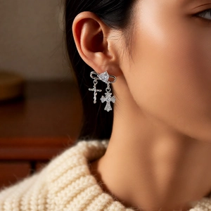 Close-up of silver zircon cross pendant hoop earring worn by a model on a soft background