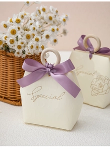 Detail of cream gift box with a wooden ring handle and a large purple satin ribbon bow